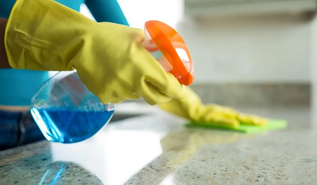 person with yellow rubber gloves spraying cleaning product on a counter and wiping it down
