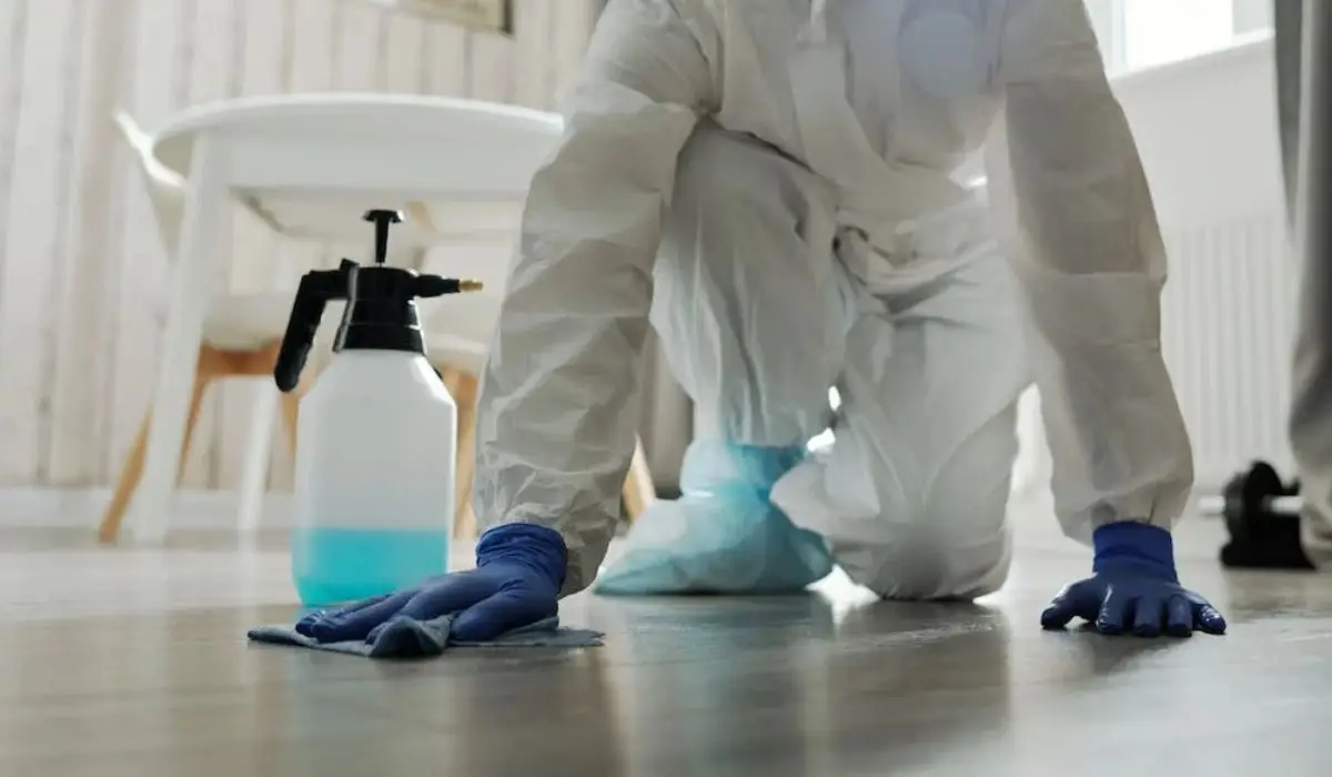 a woman in white PPE wiping the floor while wearing gloves