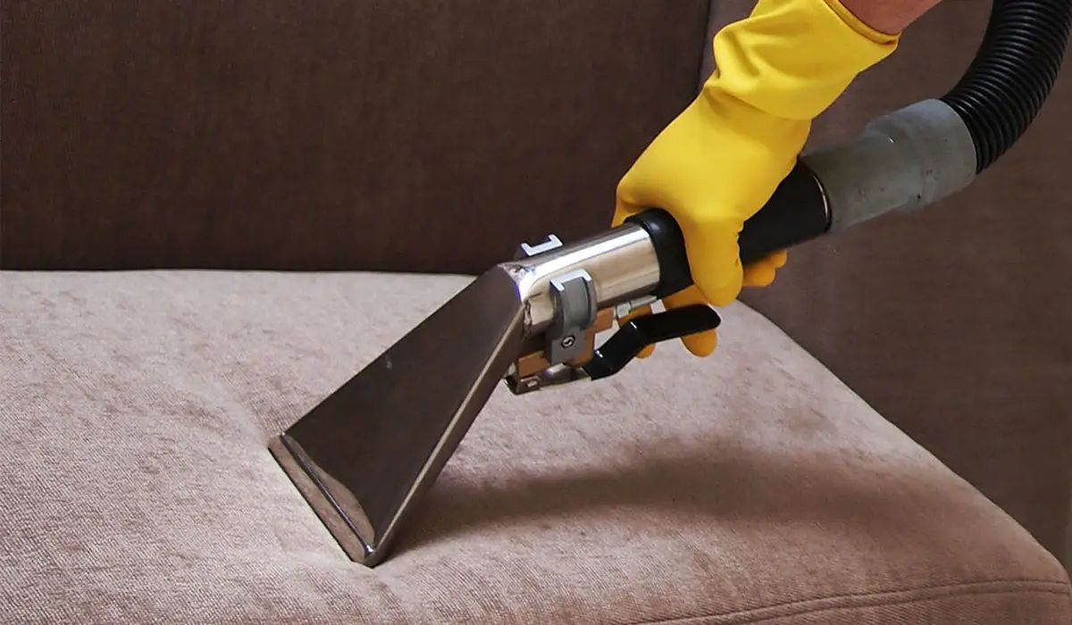 a hand wearing yellow rubber glove vacuuming the sofa surface