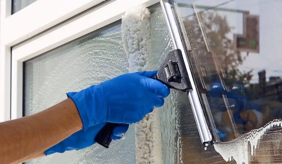 man wearing blue rubber gloves wiping the glass window with a squeegee