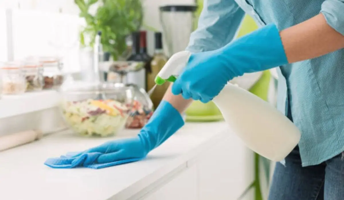 a woman wearing blue rubber gloves and cleaning the table surface